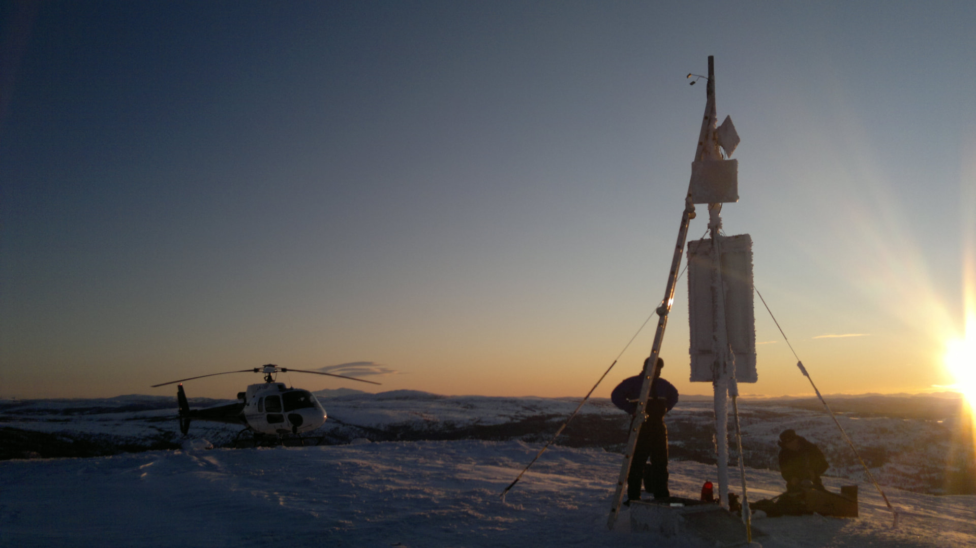Helikopter og mastearbeid på vinterfjellet i lav sol